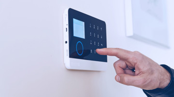 Een hand drukt op een digitaal bedieningspaneel met knoppen voor een alarmsysteem aan de muur.