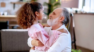 Een volwassene houdt een kind in zijn armen, terwijl ze elkaar liefdevol aankijken in een huiselijke setting.