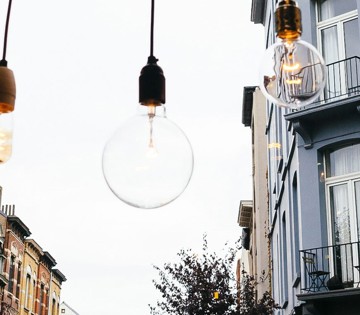 Drie hanglampen met verschillende ontwerpen in een stadsstraat, met een grijze lucht op de achtergrond.