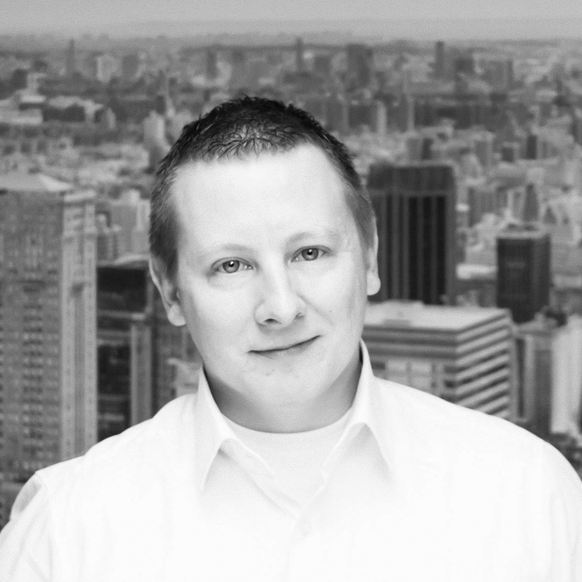 Een persoon in een wit overhemd staat voor een stedelijk landschap met hoge gebouwen op de achtergrond.