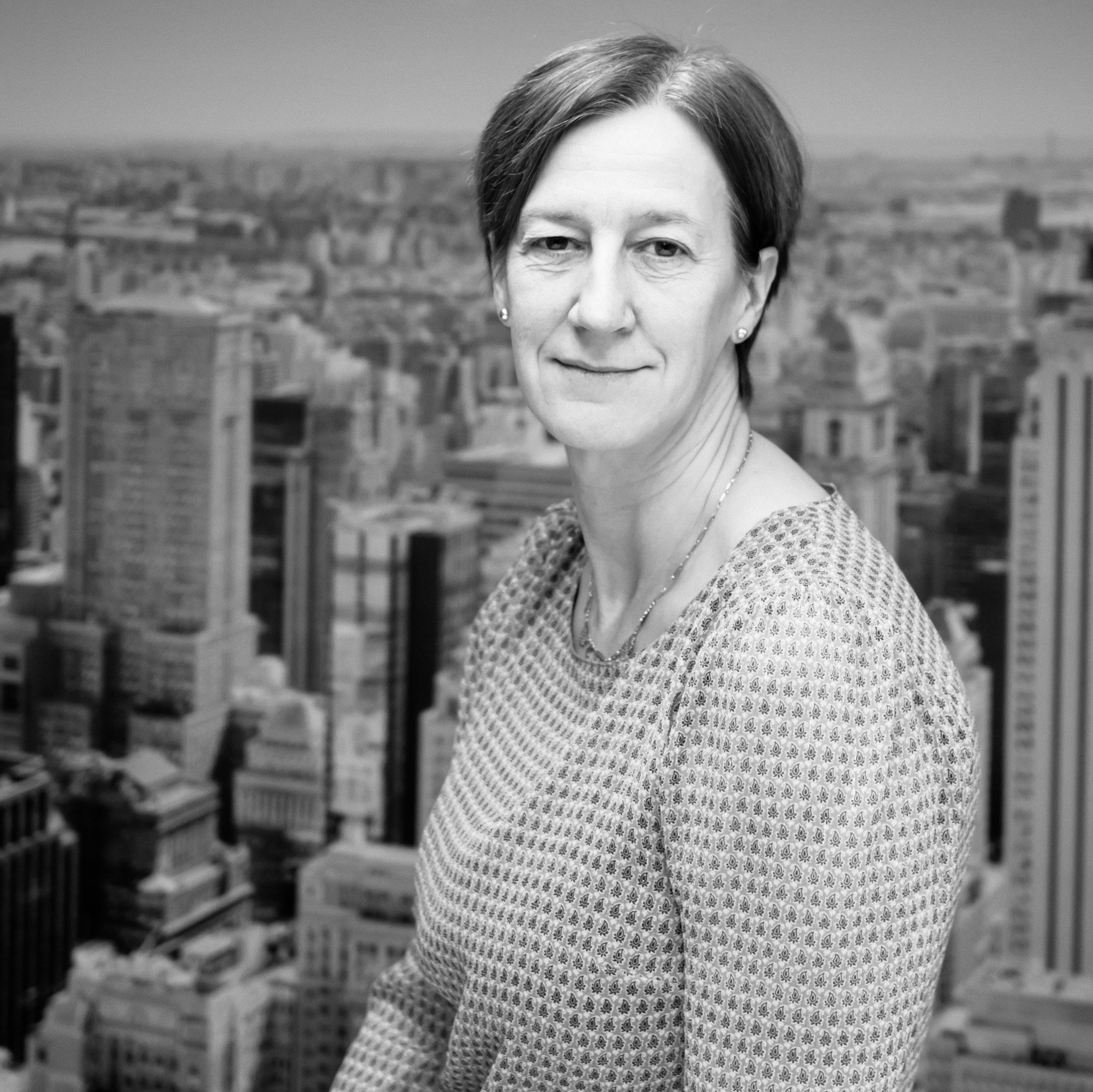 Vrouw in een grijze top, glimlachend voor een zwart-witte stadske skyline.