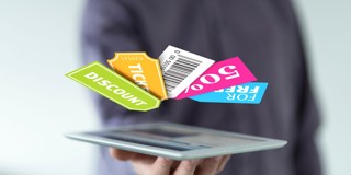 Une main tient une tablette avec des coupons de réduction et des billets flottants de différentes couleurs.