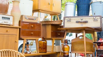 Divers meubles en bois et objets vintage sont exposés lors d'un marché aux puces, avec un accent sur un buffet en bois et une vieille valise.
