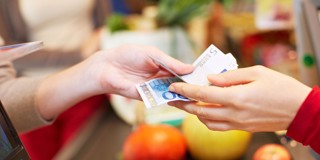 Un client paie avec des billets de banque à la caisse, entouré de légumes et de fruits.