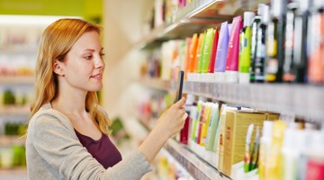Une femme choisit des produits sur une étagère remplie de divers soins et cosmétiques aux couleurs vives.