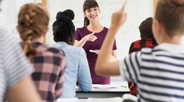 Un enseignant explique quelque chose à une classe, les élèves lèvent la main pour poser des questions.