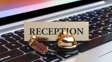 Cloche dorée de réception avec un porte-clé d'hôtel sur un clavier d'ordinateur portable, accompagnée du texte 'RECEPTION'.