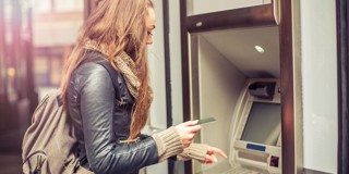 Femme aux longs cheveux, vêtue d'un blouson en cuir, touchant une carte à un distributeur automatique de billets.