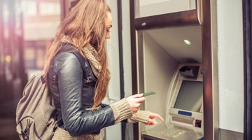 Femme aux longs cheveux, vêtue d'un blouson en cuir, touchant une carte à un distributeur automatique de billets.