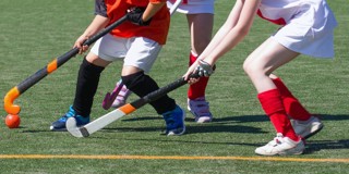 Des filles en tenue de sport jouent au hockey sur un terrain enherbé, avec un accent sur leurs crosses et le ballon.