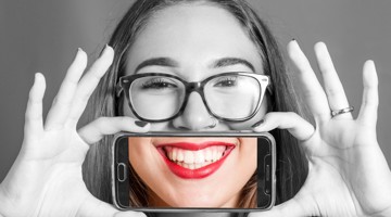 Une femme tient un smartphone devant son visage avec les deux mains, mettant l'accent sur l'appareil.