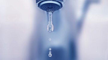 De dripping water uit een standaard kraan in een omgeving met blauwe tinten.