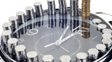 Une horloge entourée de piles de pièces de monnaie, établissant un lien visuel entre le temps et l'argent.