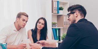 Trois personnes dans une salle de réunion, une personne explique quelque chose pendant que les autres écoutent attentivement et prennent des notes.