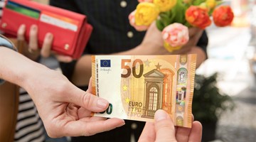 Main donnant un billet de 50 euros à une personne tenant un bouquet de fleurs.