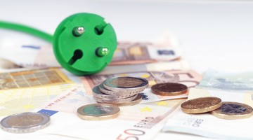 Prise verte à côté de billets de banque en euros et de pièces, symbolisant l'économie d'énergie et d'argent.