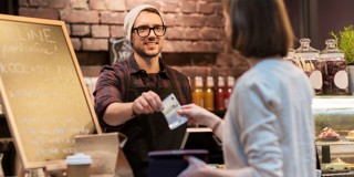 Un homme derrière le comptoir remet un reçu à une femme qui effectue un paiement dans un café.