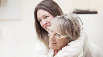 Une femme enlace une femme âgée dans une pièce claire et chaleureuse, exprimant un sentiment d'affection et de connexion.