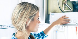 Een vrouw in een blauwe blouse stelt een verwarmingstoestel af in een lichte, moderne keuken.