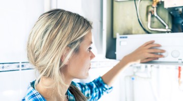 Een vrouw in een blauwe blouse stelt een verwarmingstoestel af in een lichte, moderne keuken.