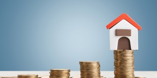 Een modelhuisje met een rood dak staat op een stapel munten, wat symbool staat voor vastgoedwaarde en investeringen.