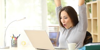 Femme les bras levés, détendue derrière un ordinateur portable, assise à un bureau avec une tasse de café et du matériel d'écriture.