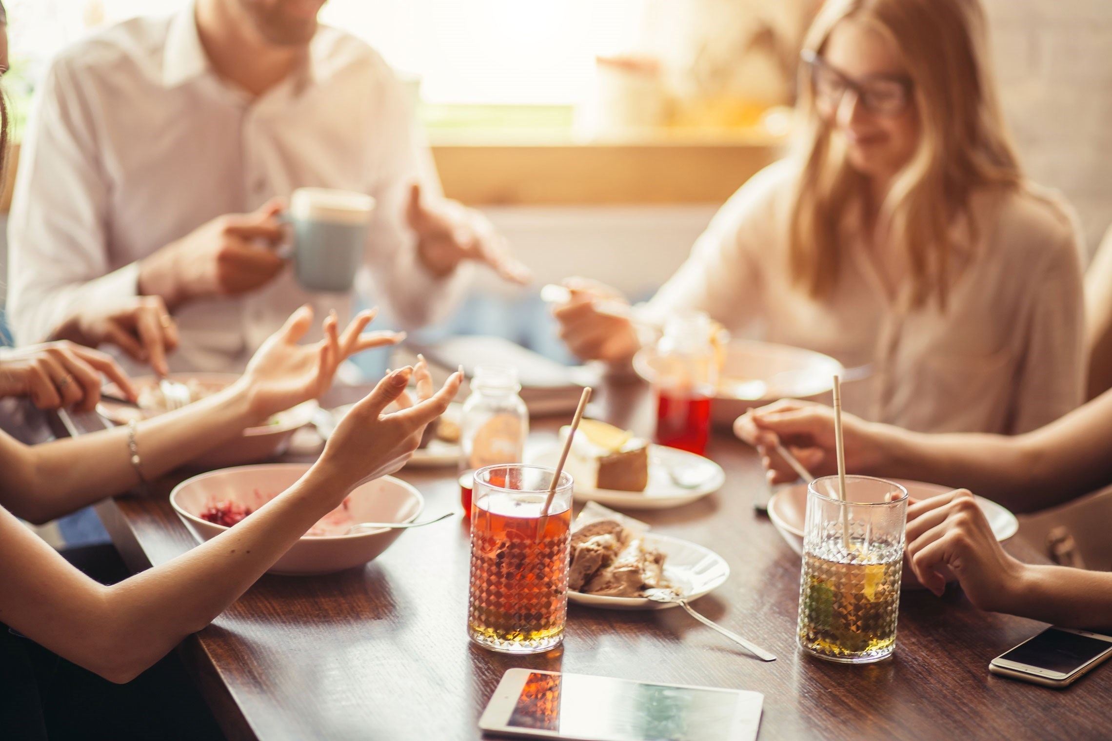 Verschillende handen van mensen die samen eten en drinken delen aan een tafel, met kleurrijke drankjes en borden vol eten.