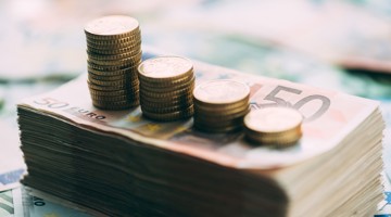 Stapels munten op gestapelde bankbiljetten, die een toenemende financiële opbrengst symboliseren.