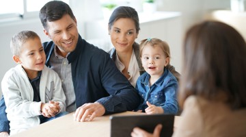 Een volwassene in een kantoor praat met een gezin met kinderen aan een tafel.