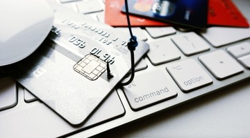 Creditcards en een muis liggen op een laptoptoetsenbord, wat wijst op online winkelen of betalingen.