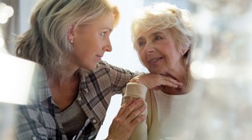 Vrouw in gesprek met een oudere vrouw in een lichte, warme en ondersteunende omgeving.
