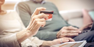 Main tenant une carte de crédit, tandis qu'un couple âgé est assis sur le canapé, regardant ensemble un ordinateur portable et un magazine.