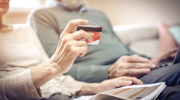 Main tenant une carte de crédit, tandis qu'un couple âgé est assis sur le canapé, regardant ensemble un ordinateur portable et un magazine.