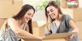 Deux femmes examinent ensemble le contenu d'une boîte ouverte entre des cartons de déménagement.