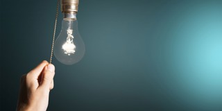 Een hand trekt aan een trekkoord van een gloeilamp voor een blauwe achtergrond, wat suggereert dat de lamp aan gaat.