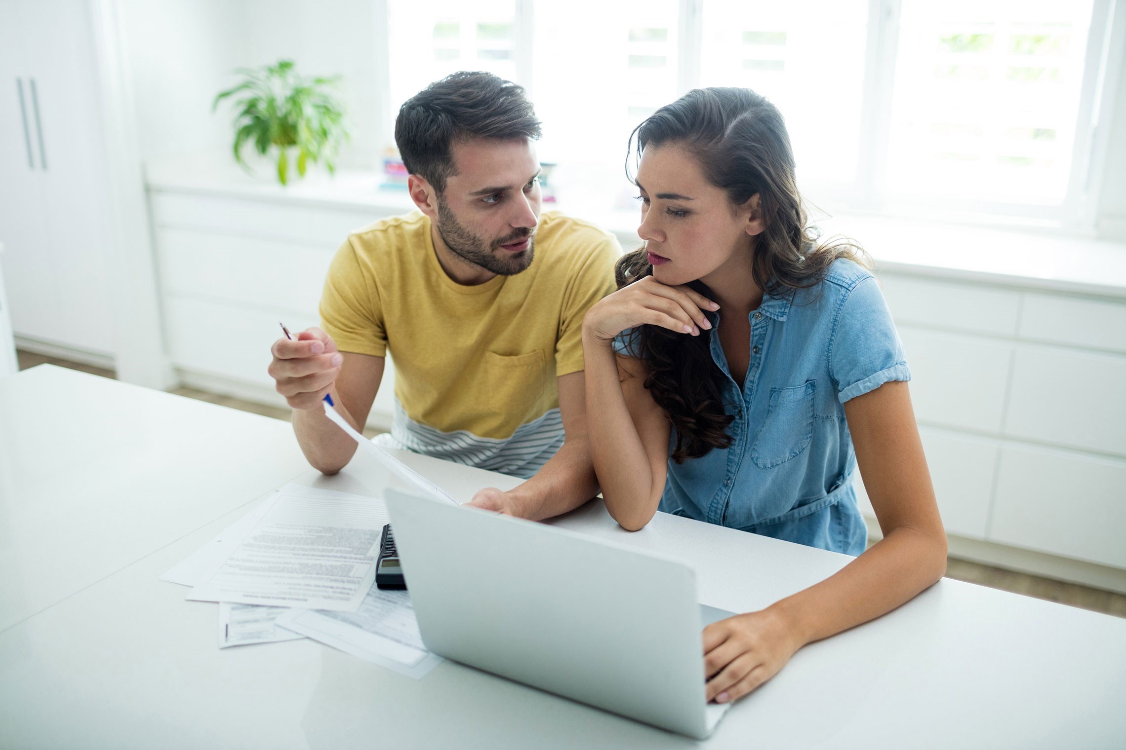Twee mensen zitten aan een tafel met een laptop en papieren, terwijl ze samenwerken aan een project of presentatie.
