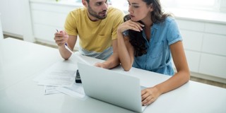 Twee mensen zitten aan een tafel met een laptop en papieren, terwijl ze samenwerken aan een project of presentatie.