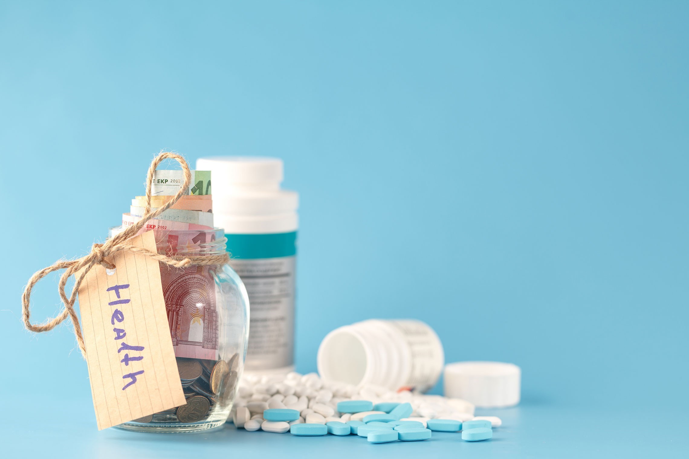 Glazen pot met geld en een label 'Gezondheid', omringd door medicijnen en pillen op een blauwe achtergrond.