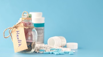 Glazen pot met geld en een label 'Gezondheid', omringd door medicijnen en pillen op een blauwe achtergrond.
