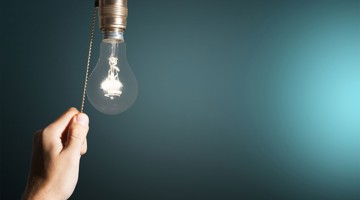 Une main tire sur une corde pour allumer une ampoule sur un fond bleu-vert.