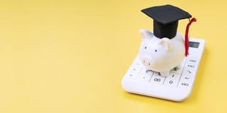 Un cochon tirelire blanc avec un chapeau de diplômé est posé sur une calculatrice, sur un fond jaune.