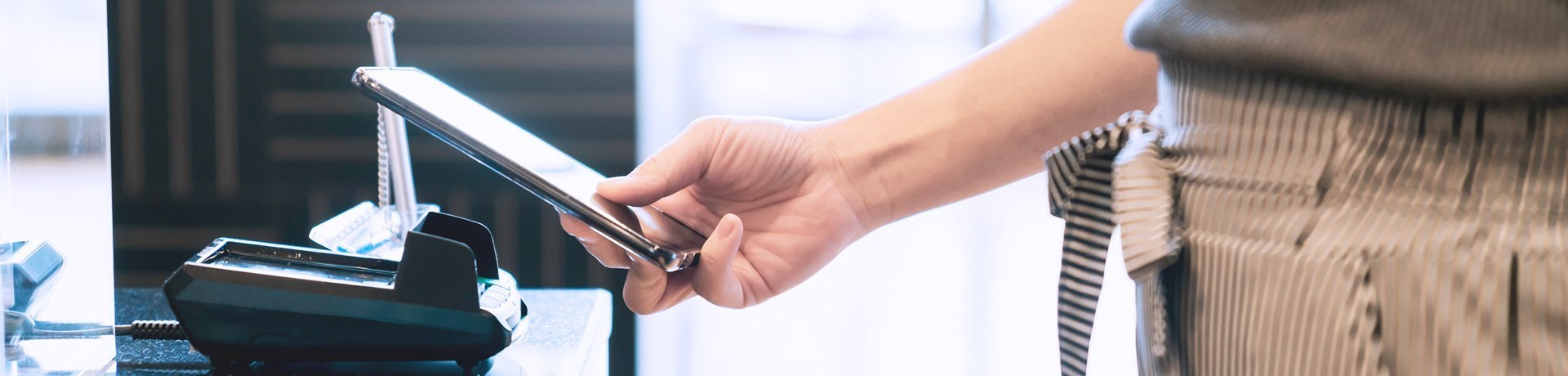 Een hand houdt een smartphone boven een zwarte smartphonehouder op een bureau.