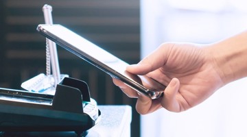 Een hand houdt een smartphone boven een zwarte smartphonehouder op een bureau.