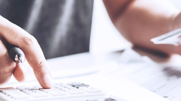 Hand die een rekenmachine gebruikt, terwijl de andere hand een creditcard vasthoudt.