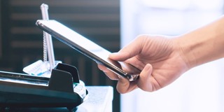 Une main tient un smartphone au-dessus d'un chargeur sans fil sur un bureau.