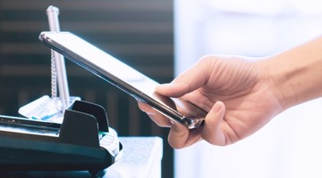 Une main tient un smartphone au-dessus d'un chargeur sans fil sur un bureau.