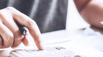 Main utilisant une calculatrice avec un stylo dans l'autre main, concentrée sur des calculs.