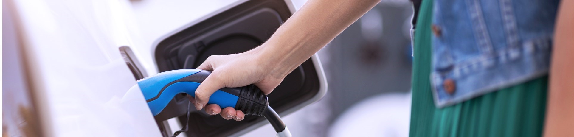 Une main tenant un câble de recharge bleu en train de recharger une voiture électrique à une station de recharge.
