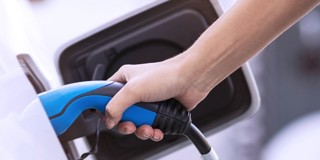 Une main tenant un câble de recharge bleu en train de recharger une voiture électrique à une station de recharge.