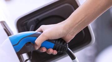 Une main tenant un câble de recharge bleu en train de recharger une voiture électrique à une station de recharge.